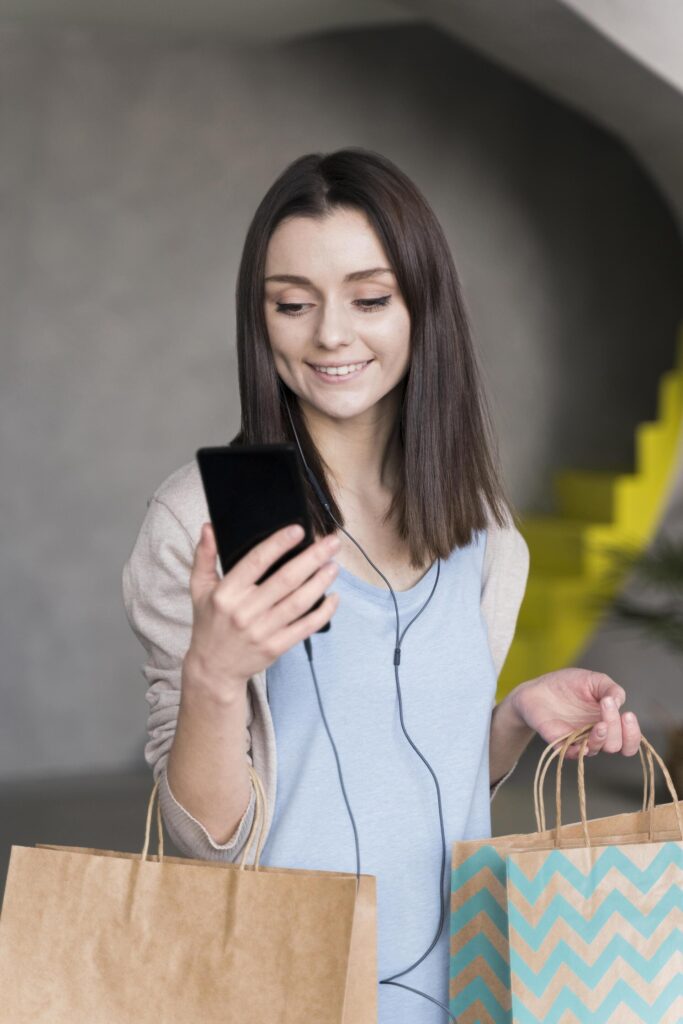 front view smiley woman holding smartphone paper bags (1) (1)